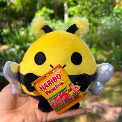 Peluche de abeja amarillo y negro acompañado de una golosina en la foto.