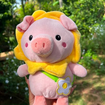 Peluche de cerdito rosa con capucha amarilla y un lazo.
