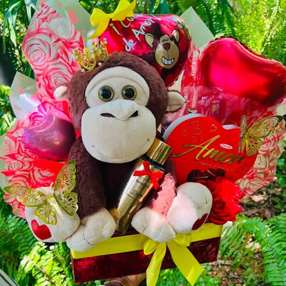 Cesta de regalo con monito de peluche, flores y globos de corazón.