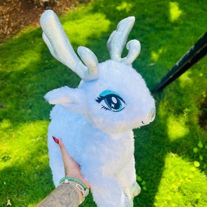 Peluche de ciervo blanco con astas y detalles azules en los ojos.