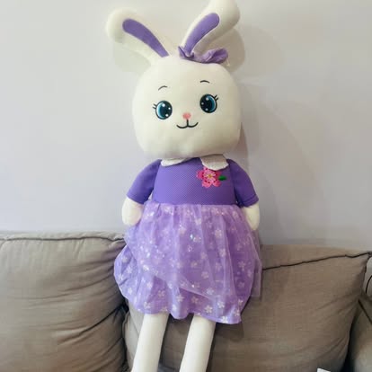 Peluche de conejita blanca con vestido morado y lazo entre las orejas.