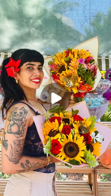 Mujer con una flor roja en el cabello sosteniendo ramos de girasoles y flores de colores.