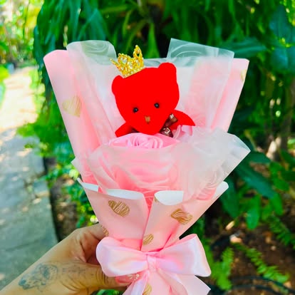 Peluche rojo de Hello Kitty con corona, flor rosada y envoltura en tonos rosa.