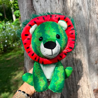 Peluche de león verde con melena roja inspirada en una sandía.