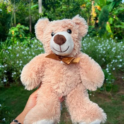 Peluche de osito beige con un lazo en el cuello.