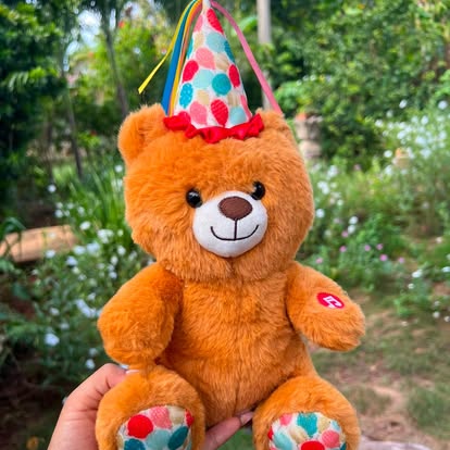 Peluche de osito naranja con gorro de fiesta de lunares.