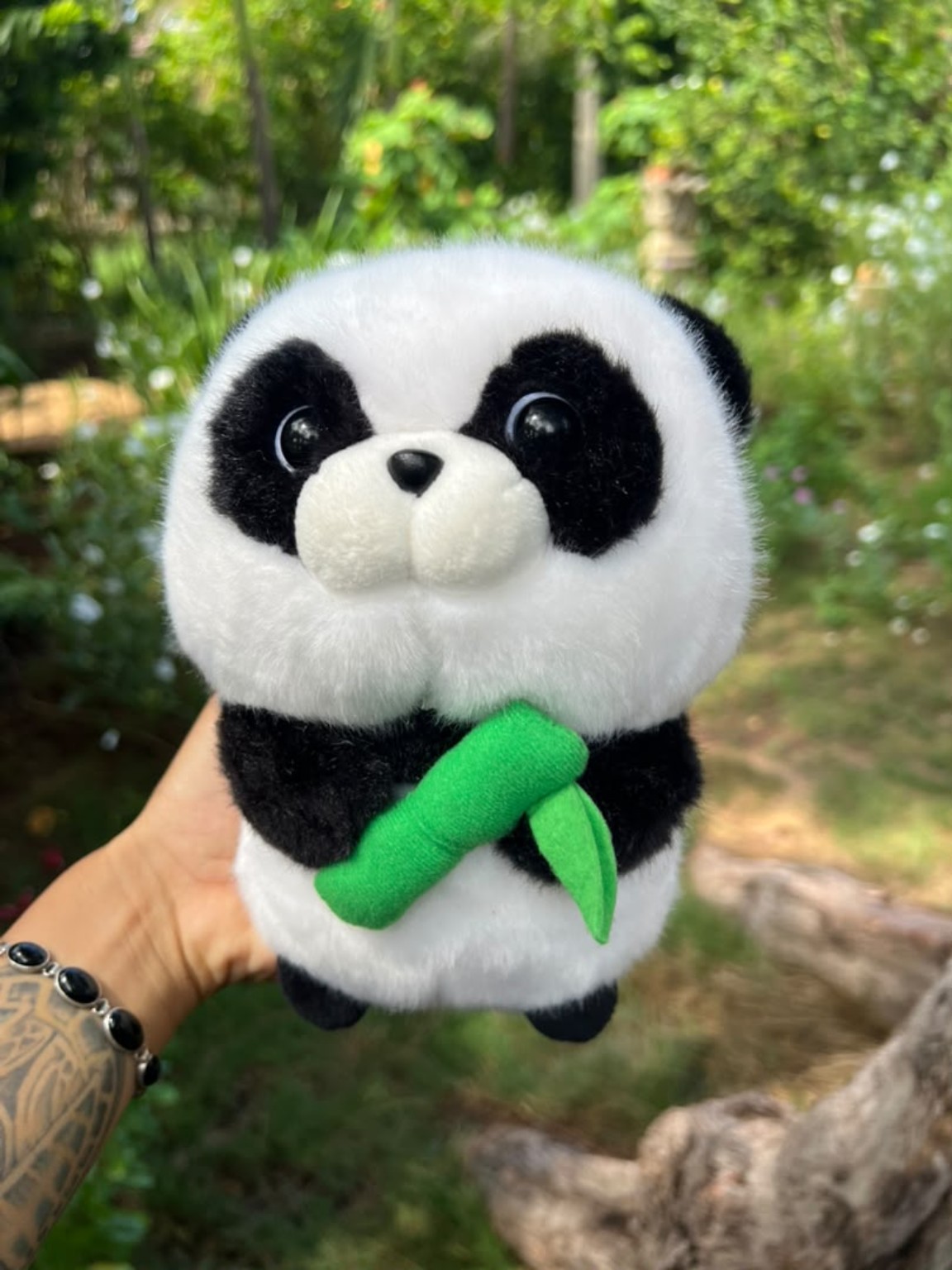 Peluche de panda blanco y negro con un detalle verde de bambú.