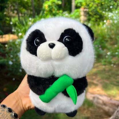 Peluche de panda blanco y negro con un detalle verde de bambú.