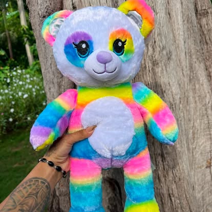 Peluche de panda con colores de arcoíris y detalles blancos.