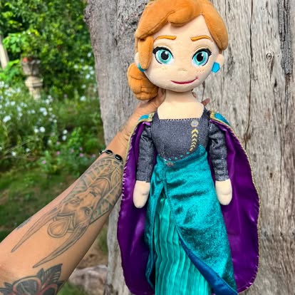 Muñeca de peluche de Anna, con vestido azul verdoso y capa morada.