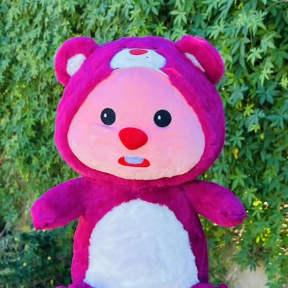 Peluche de rostro rosa y traje morado con capucha de orejitas.