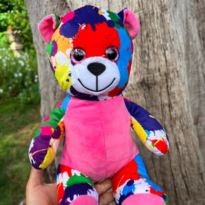 Peluche de perrito con manchas de colores y barriga rosa.