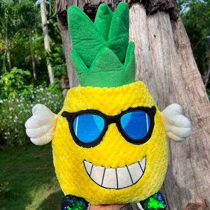 Peluche amarillo con forma de piña, gafas azules y sonrisa.
