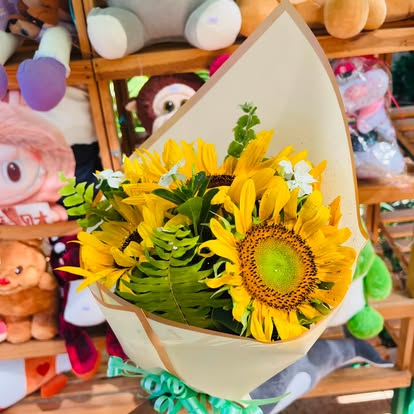 Girasoles con follaje, pequeñas flores claras y envoltura color crema.
