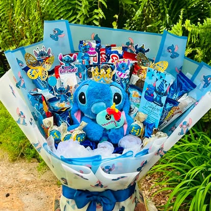 Peluche de Stitch rodeado de dulces y detalles azules, con envoltura temática.