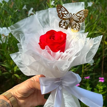 Rosa roja con mariposa dorada, envoltura blanca y lazo claro.