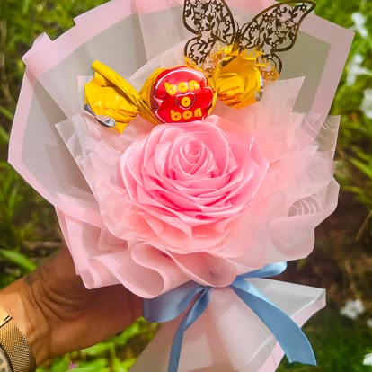 Rosa decorativa rosada con bombón, mariposa dorada y lazo azul.