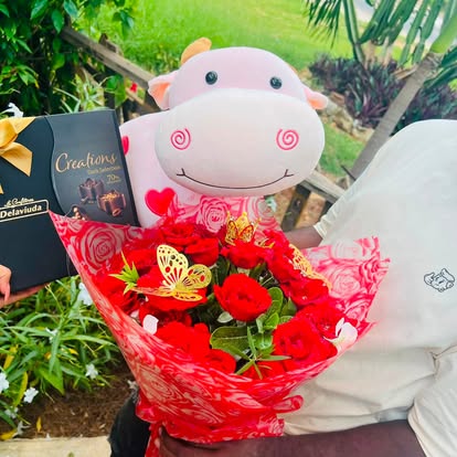 Ramo de rosas rojas con una vaquita de peluche y galletas, en envoltura clara y roja.