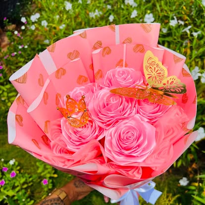 Ramo de flores decorativas rosadas con mariposas doradas y envoltura rosa.