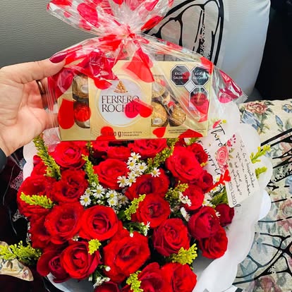 Ramo de rosas rojas y pequeñas flores blancas acompañado de una caja de bombones.