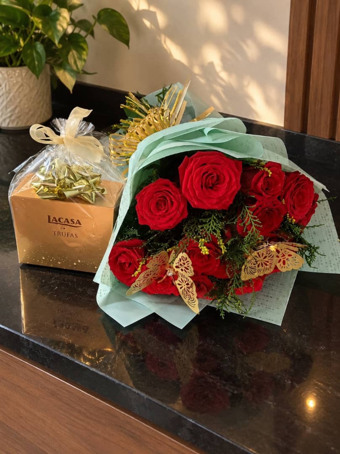 Rosas rojas con envoltura verde menta, mariposas doradas y una caja de trufas.