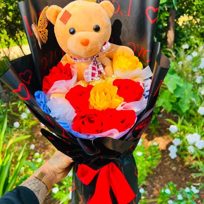 Ramo con osito de peluche y rosas rojas y amarillas, en envoltura negra.