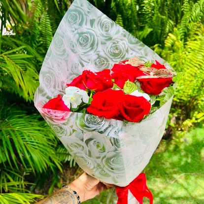Ramo de rosas rojas y blancas con envoltura clara estampada y lazo rojo.