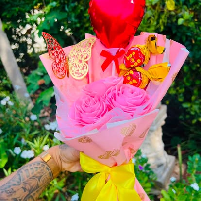 Ramo de flores rosadas con bombones, mariposas y un globo rojo de corazón.
