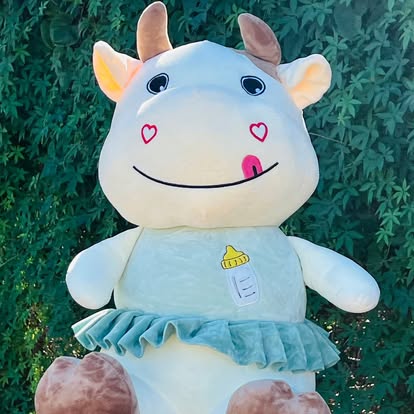 Peluche de vaquita clara con falda azul y pequeños corazones en la cara.
