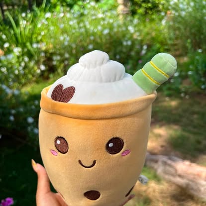 Peluche con forma de vaso de bebida, rostro sonriente y pajita verde.